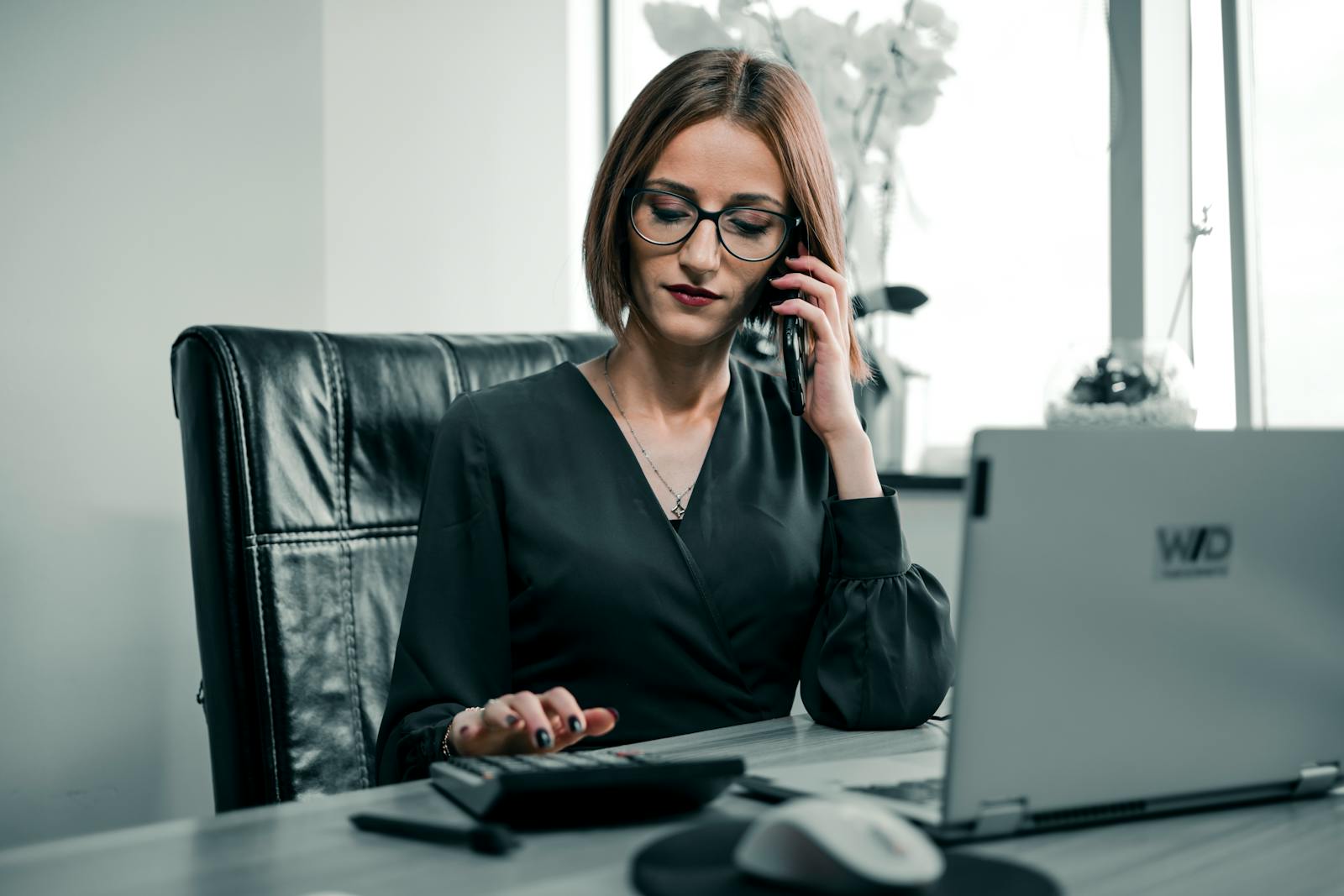Photo by Wolrider YURTSEVEN Businesswoman multitasking with a phone and calculator at a desk, showcasing office productivity.